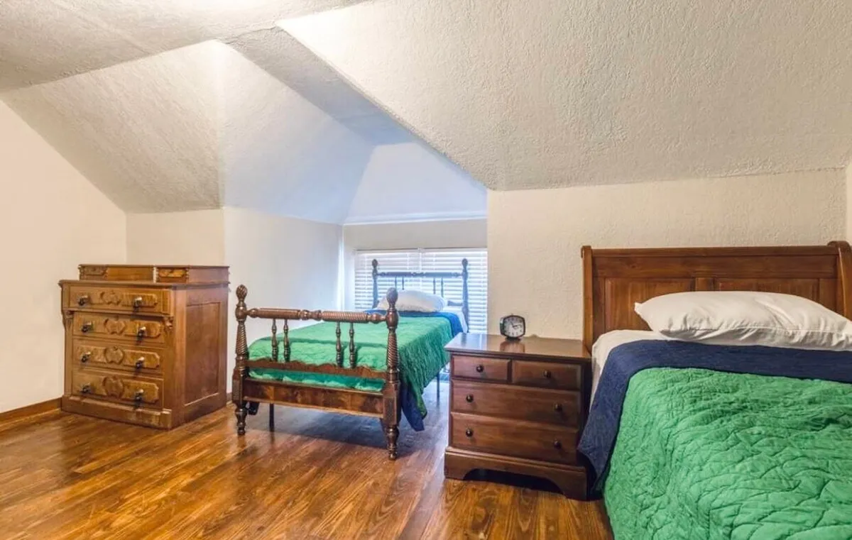 This image features two neatly made beds, a solid wooden dresser, and a nightstand. The room is softly lit and feels inviting, offering ample sleeping arrangements for multiple guests. The setup suggests flexibility for families or friends traveling together, with a layout that promotes comfort and relaxation.