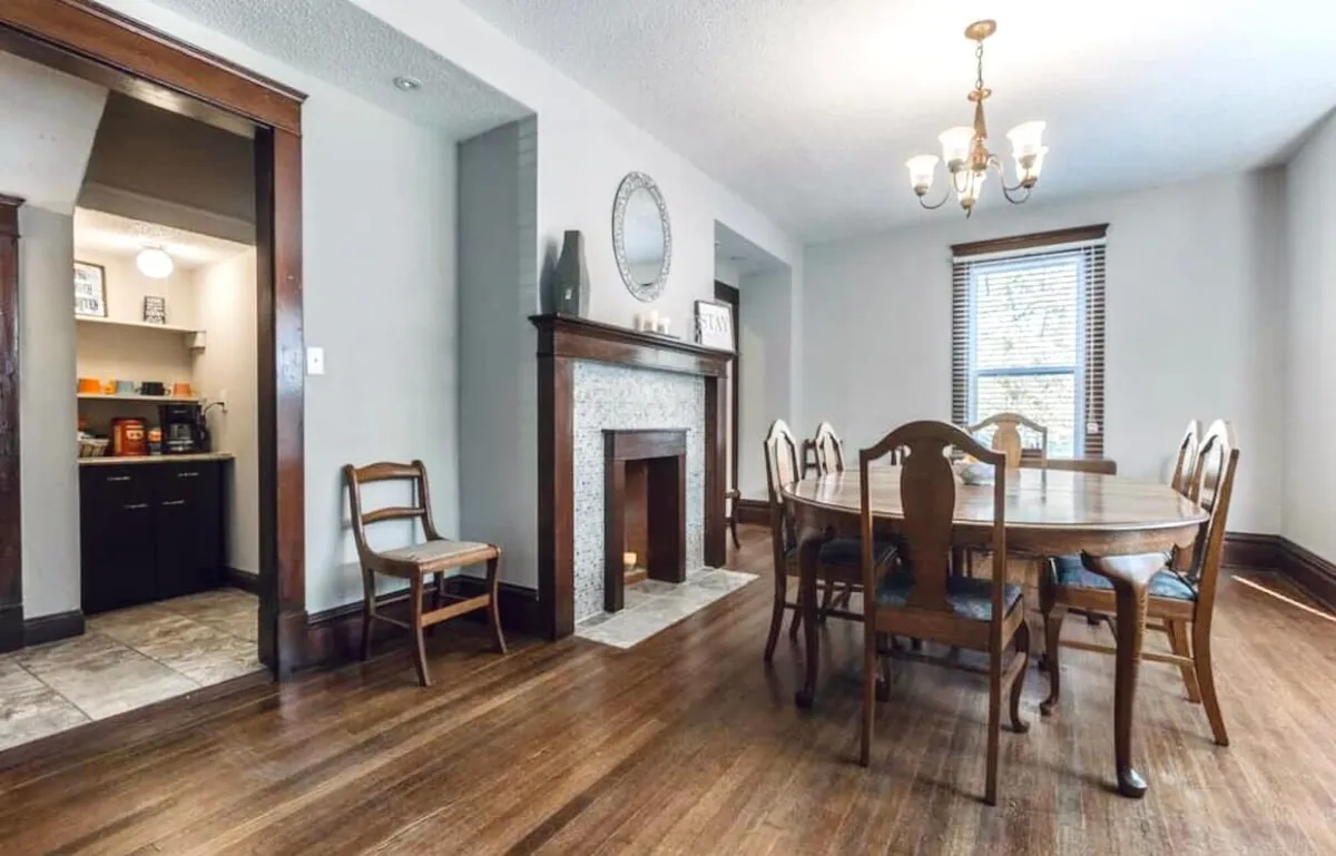 A bright and inviting dining area featuring a wooden table, a classic fireplace, and large windows letting in ample natural light. The setup suggests a space ideal for gathering before venturing out or sharing stories after exploring the city.