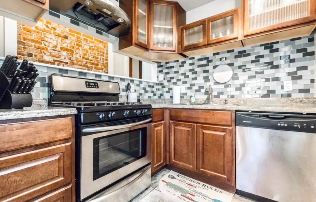 A modern kitchen with a stainless steel stove, granite countertops, contemporary backsplash, and wood cabinetry. The scene exudes a warm, functional vibe and suggests the space is ideal for both everyday cooking and special occasions.